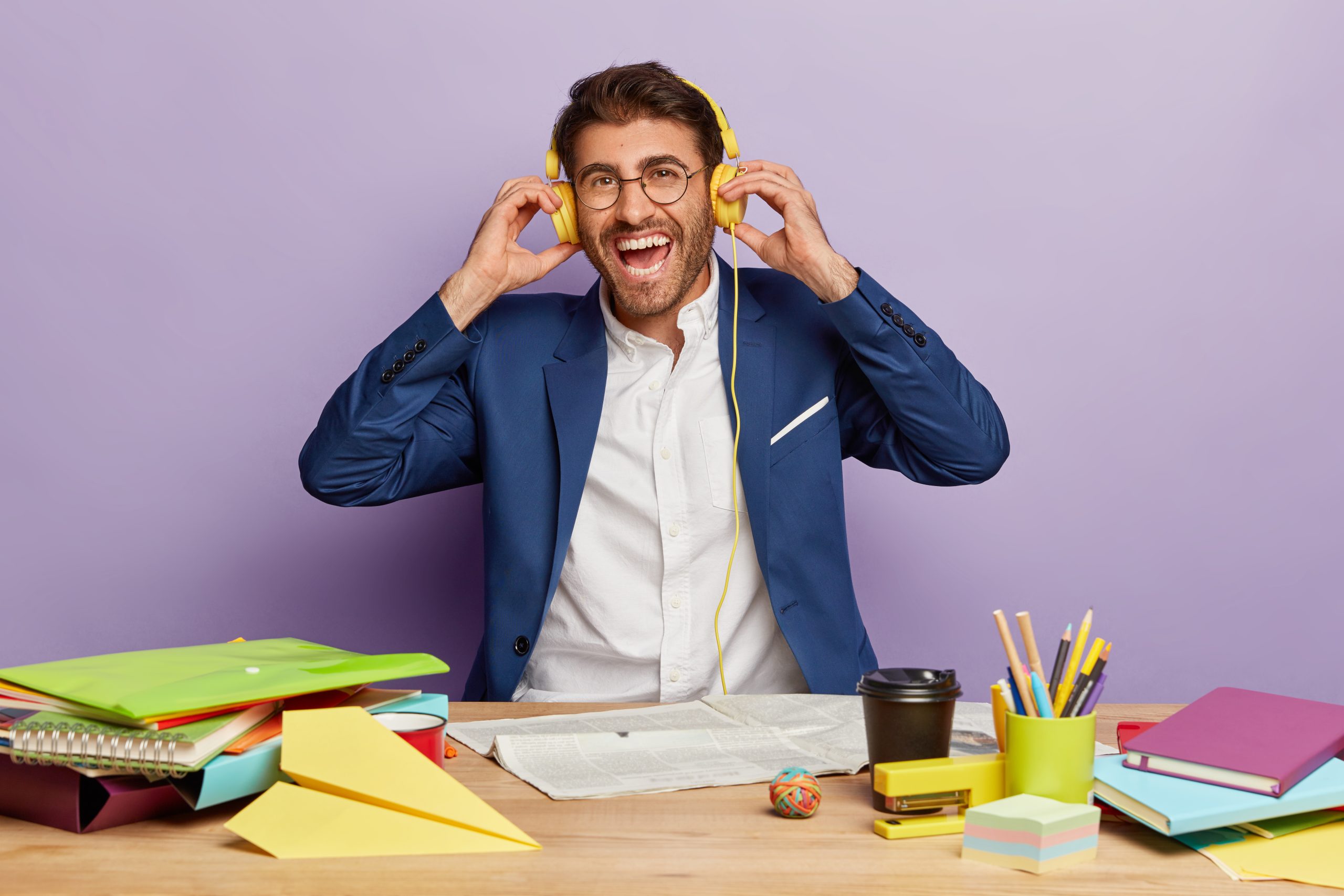 Positive boss in classy elegant suit listens music in headphones, enjoys break, has happy expression. Glad businessman listens online conference in office. Happy student gets education on internet